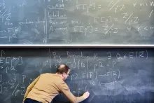 A mathematician writing a proof in chalk on a blackboard covered with equations.