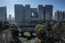 Aerial photograph of the modern office towers housing DeepSeek's headquarters across a river with an arched bridge in the foreground.