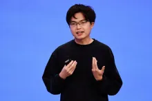 Photograph of Moonshot AI founder Yang Zhilin speaking on stage against a blue background.