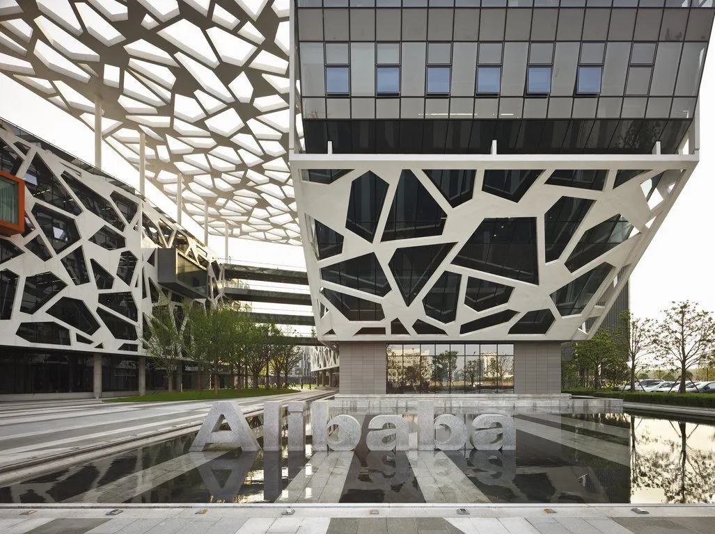 Photograph of Alibaba headquarters in Hangzhou, showing the Alibaba name in stone reflected in a plaza pool in front of the building.