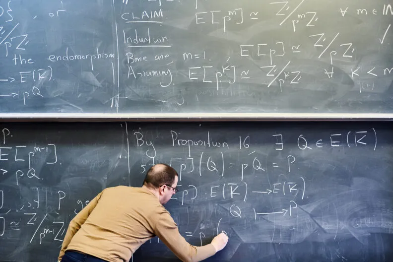 A mathematician writing a proof in chalk on a blackboard covered with equations.